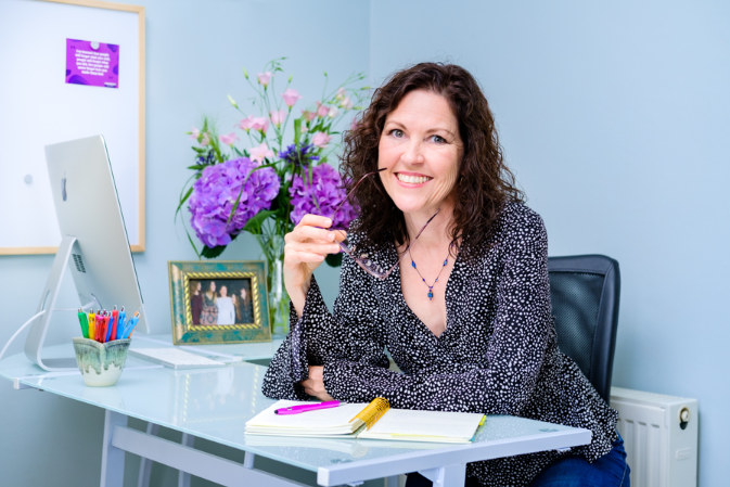 marypat in her office with purple hydrangeas ina vase behind her.